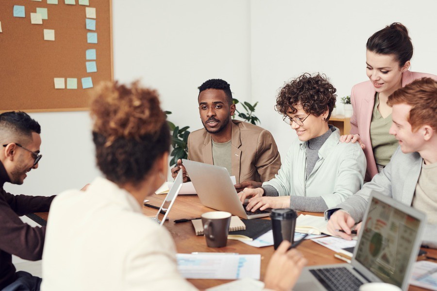 An office team sits around a shared table, laptops open. 